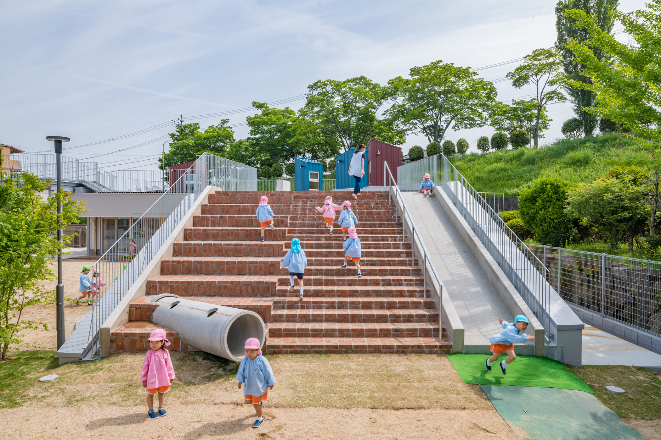 レンガ敷き大階段、滑り台、土管が園児の心を掴む、建築の立体的遊具化。